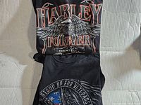 Two Harley Davidson T-shirts laid flat showing front graphic prints. One is XL size with 'Harley Forever' eagle design and the other is 2XL with a different eagle Harley print.