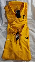 Two yellow Nike polo shirts featuring Pittsburgh Pirates logo, both folded and stacked showing tags.