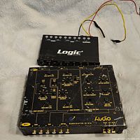 Top view of Planet Audio crossover and Logic EQ placed on white surface with attached wires, showing labeled controls and ports