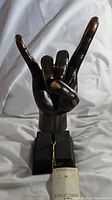 Front view of bronze-colored hand sculpture on black base, showing 'rock on' hand gesture.