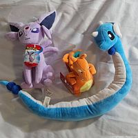 Lot of three vintage Pokemon plush beanies including Espeon, Charizard and Dragonair. Espeon and Charizard shown with original Pokemon tags attached.