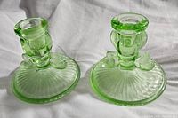 Photo of two greenish-yellow Vaseline glass candle holders featuring koi fish figures on base, showing overall design and condition.