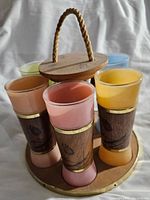 Side view of six colored tiki glasses with wooden wrap and round wooden carrier with rope handle