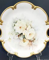 Full top-down view of floral charger plate showing central white and cream rose design with subtle green leaves and gold trim around edge and handles.