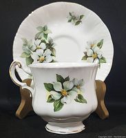 Tea cup in front, saucer behind, showing dogwood floral pattern and gold accent details