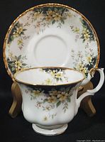 Tea cup displayed at an angle showing floral pattern with yellow and white flowers and gold trim.