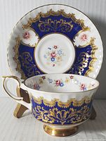 Tea cup with cobalt blue and gold detailing, floral pattern inside and out, with matching saucer in background.