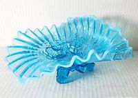 Photo showing the vintage blue opalescent glass bowl from an angled view highlighting the ruffled edge and hobnail pattern.