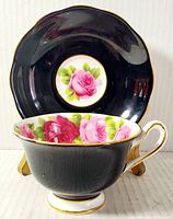 Photo of tea cup in front of saucer showing front side with floral interior and gold trim on handle and rim