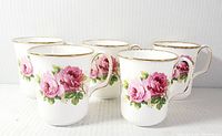 Front angled view of the five coffee mugs displaying rose floral designs and gold rim details.