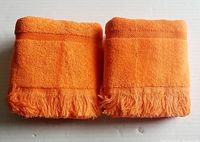 Two neatly folded bright orange guest towels stacked side by side showing fringed ends and decorative banding.