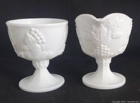 Front view of milk glass creamer and open sugar bowl showing raised grape cluster and leaf pattern details, both on pedestal bases.