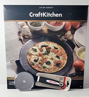 Boxed Craft Kitchen ceramic pizza stone with a built pizza on it and the pizza cutter shown in front.
