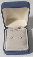 Pair of small round 14K gold stud earrings in an open blue velvet jewelry box with cream-colored interior and 14KT. GOLD marking.