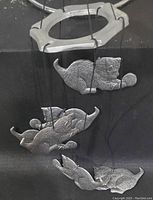 Front view of the metal wind chime showing four cats playing with yarn balls, suspended vertically with hooks and strings.