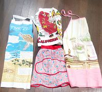 Four vintage aprons laid out flat showing diverse colorful prints and designs