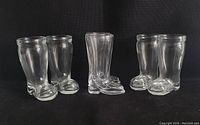 Four vintage clear glass boot-shaped shot glasses and two clear glass cowboy boots displayed against a black background