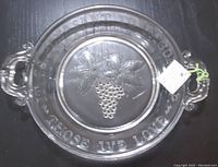 Top view of antique clear pressed glass serving plate showing grape cluster design and inscription around edge.