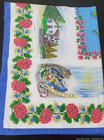 Photo showing full view of the tablecloth with colorful scenic house and floral border design laid flat.