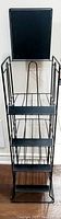 Front view of the black wrought iron vintage magazine stand showing three tiered wire racks and solid back panel