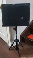 Front view of the adjustable music stand showing the solid flat music holder and tripod base.