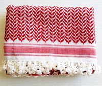 Folded vintage tablecloth showing red and white geometric pattern with white chunky fringe along edge.