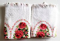 Pair of vintage unused white guest towels with pink and red floral design and fringed edges, folded and stacked.