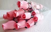 Close up of light pink wooden artificial roses wrapped in clear plastic with white floral print.