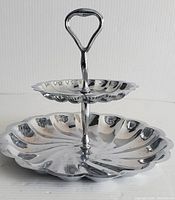 Front view of two-tier chrome server showing scalloped edges and handle.