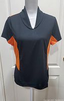 Full front view of black athletic top with orange side panels on a dress form.