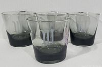 Four smokey black lowball glasses with weighted base arranged in a diamond shape, each engraved with a letter "W" monogram.