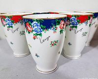 Front view of the seven Kenzo AITO Japan porcelain cups showing the floral pattern, gold trim, and Kenzo signature.