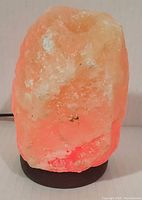 Front view of the lit Himalayan salt lamp showing pinkish-orange glow and rough natural crystal texture