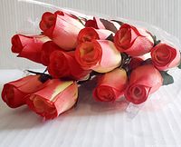 Cluster of 24 artificial wooden roses in orange and yellow colors wrapped in clear plastic, showing rounded petals and green fabric leaves.