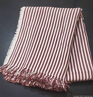 Folded red and white striped beach blanket or throw with fringed edges on dark surface.