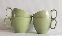 Four stacked light green melamine cups with squared handles, showing their shape and color.