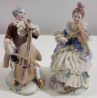 Front view of male and female musicians porcelain figurines, detailed period costumes, seated on decorated bases