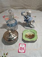 Overall shot of four antique items showing vinegar/sauce dish with glass stopper, figurine, green dish with scenic decal, and crystal chutney dish with lid.