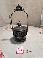 Full view of entire antique pickle castor with handle, lid featuring swan finial, ruby red glass body, silver base, and fork attached to handle.