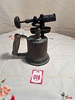 Full side view of the antique metal gas blow torch showing cylindrical tank, wooden handle, and burner assembly.