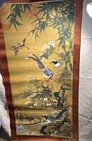 Full view of the Asian scroll painting showing bamboo, flowers, and birds with brown fabric border.