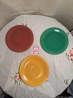 Photo showing three colorful round Fiestaware dinner plates on a floral tablecloth, showcasing red, green, and yellow plates.