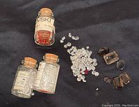 Overview of glass bottles with rhinestones and cubic zirconia stones alongside loose colored faceted stones on black background