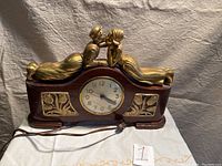 Full view of the wooden mantle clock with kissing couple sculpture on top, showing the clock face and wooden body.