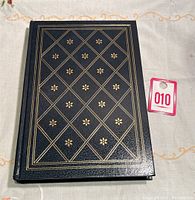 Front cover of the hardcover book showing black simulated leather with gold embossed geometric pattern and floral designs.