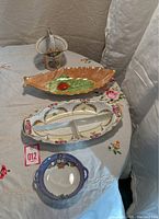 Four Noritake Lustre 1930s porcelain pieces displayed on a white embroidered tablecloth, showing overall condition and colors.