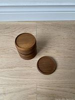 Stack of 12 mid-century teak drinking coasters with one coaster lying flat to show shape and finish.