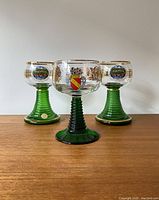 Front photo of 3 vintage German wine glasses with green stems and decorative bowl painting.