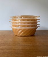 Side view of stack of five amber swirl Fire King small casseroles showing shape and pattern