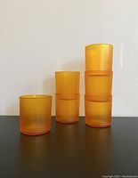 Six amber-colored melamine drinking glasses arranged in stacks and rows, showing their shape, texture, and color.